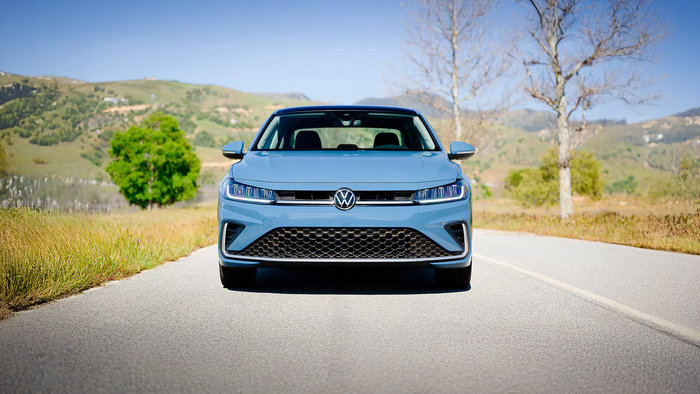 Front view of a blue Volkswagen Jetta driving on a road.